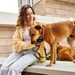 Why My Dog is Walking Slow with Head Down? Expert Insights A charming young smiling girl is resting on a bench while walking with two golden dogs. The girl